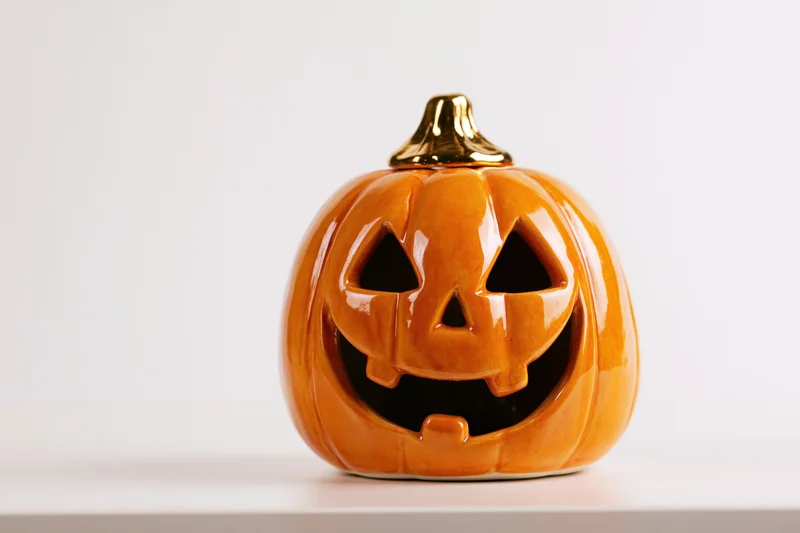 Ceramic jack-o-lantern decoration with carved smiling face and gold stem on white surface