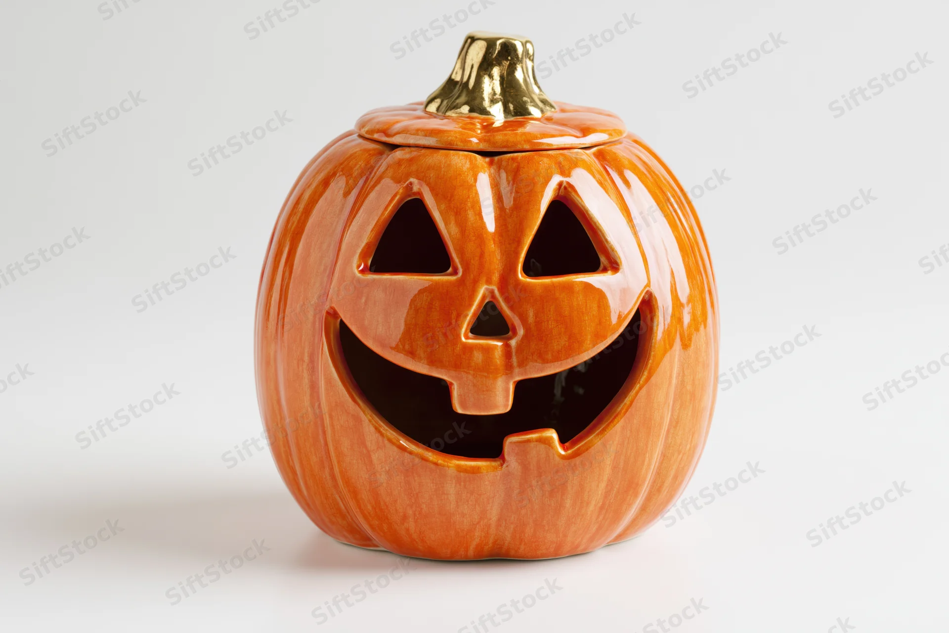 Ceramic jack-o-lantern decoration with smiling carved face and gold stem on white background