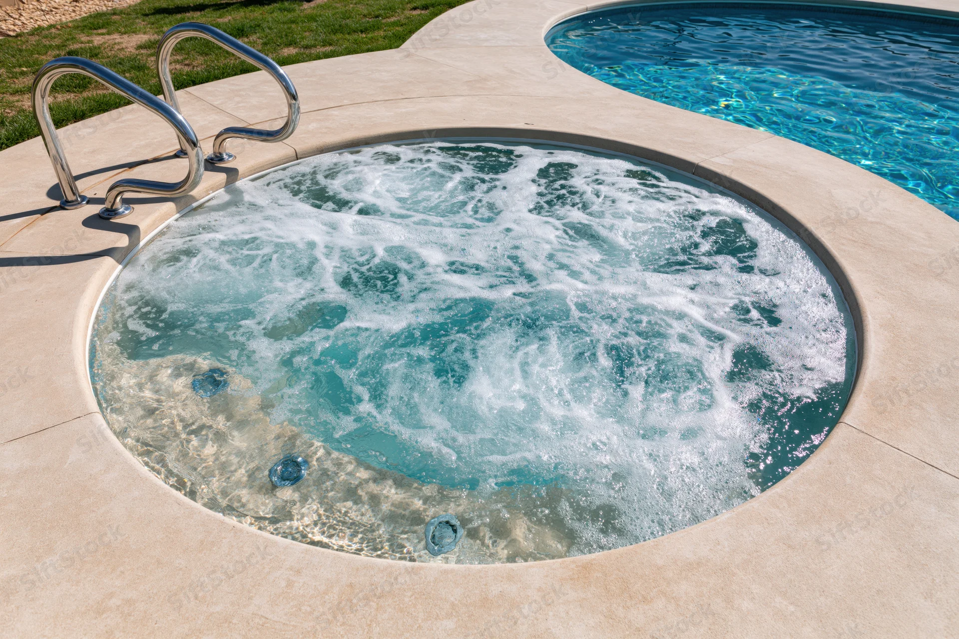 Circular hot tub with bubbling jets set into a concrete patio beside a swimming pool