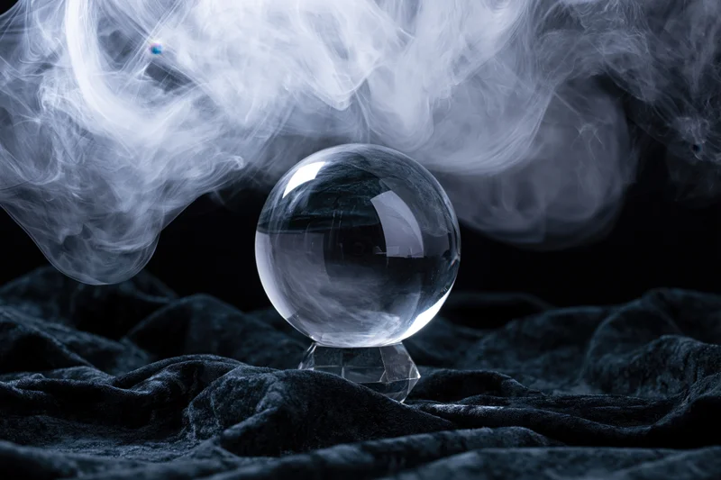 Crystal ball resting on a crystal base with swirling smoke above on dark velvet fabric