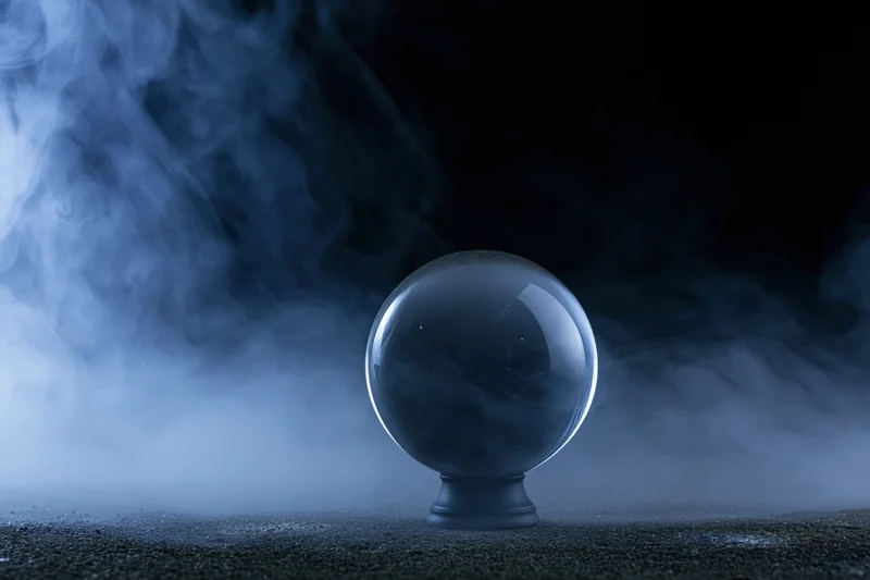 Clear glass crystal ball on dark pedestal surrounded by swirling blue smoke in dim studio setting