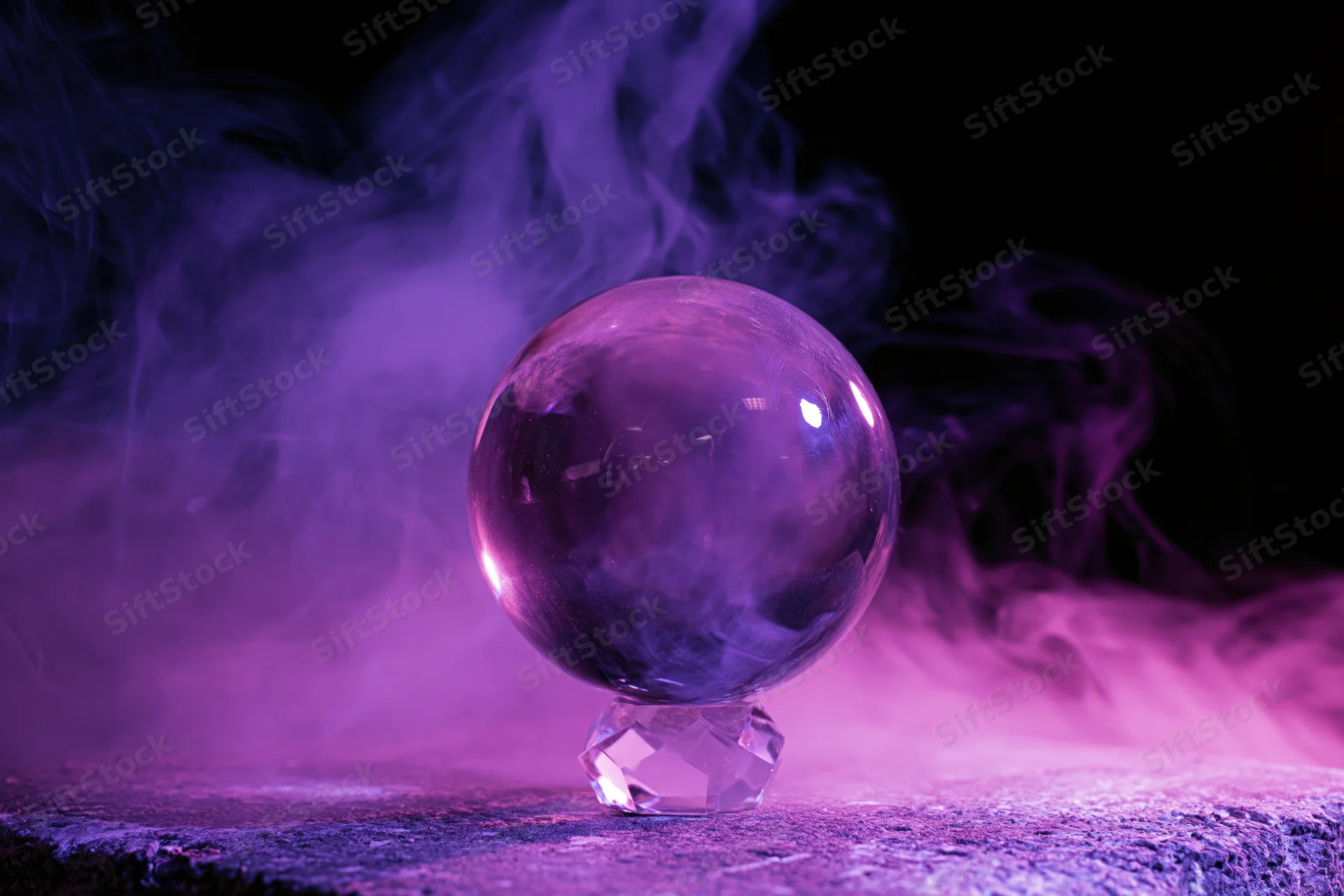 A clear glass crystal ball on a faceted crystal base surrounded by purple smoke in a dark studio setting
