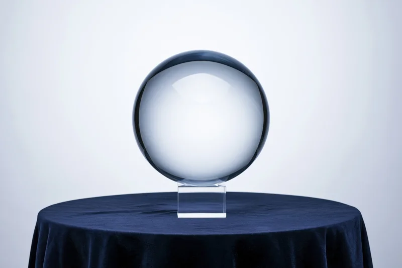 Clear glass crystal ball on a transparent acryl stand atop a navy velvet-covered table in a studio setting