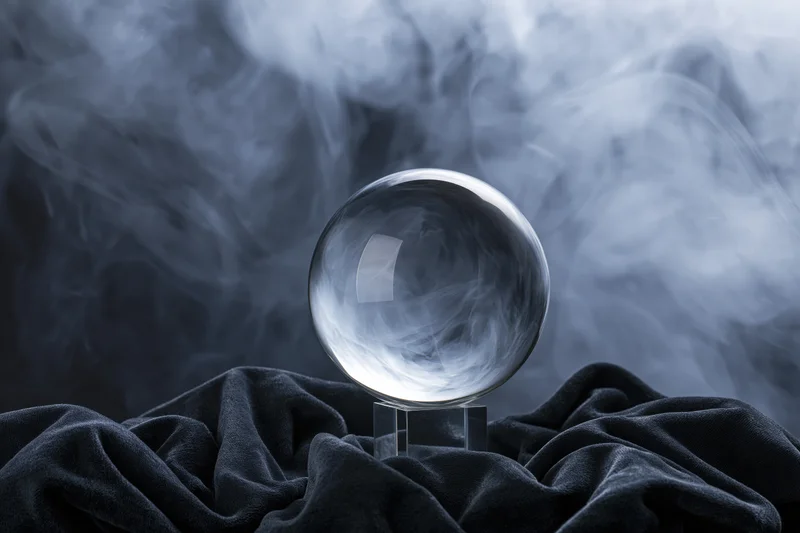 Crystal ball resting on a transparent stand atop dark fabric with swirling smoke in the background
