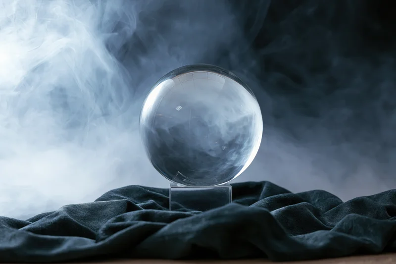 Clear glass crystal ball on transparent acryl stand surrounded by smoke on dark velvet fabric