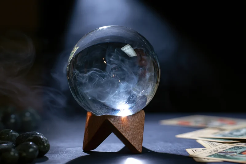 Crystal ball with swirling smoke on wooden stand beside tarot cards on dark surface