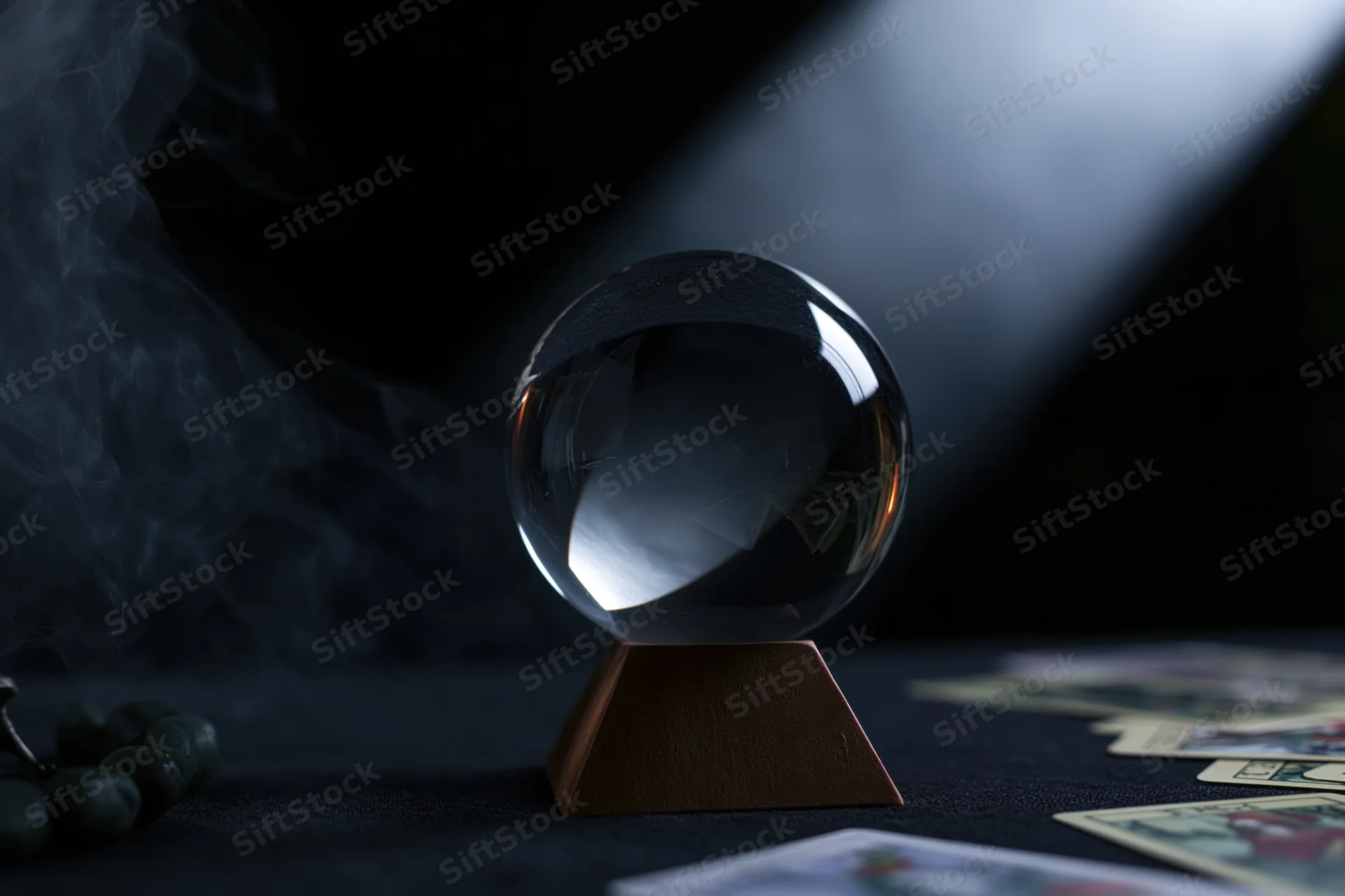 Crystal ball on wooden base surrounded by tarot cards and smoke on dark surface