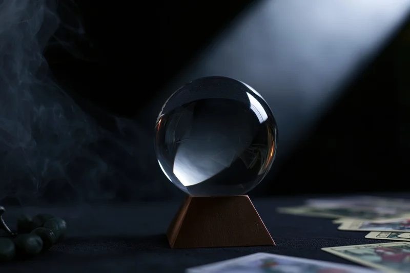Crystal ball on wooden base surrounded by tarot cards and smoke on dark surface