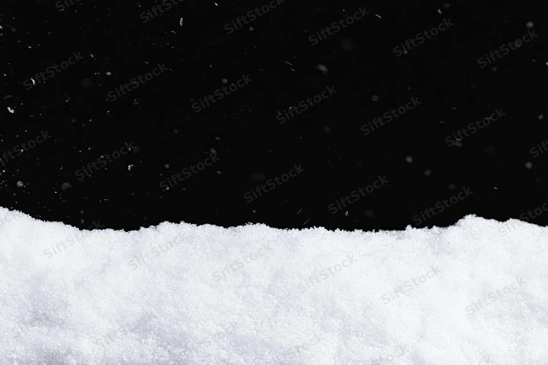 Close-up flat lay of snow surface with falling flakes against black background