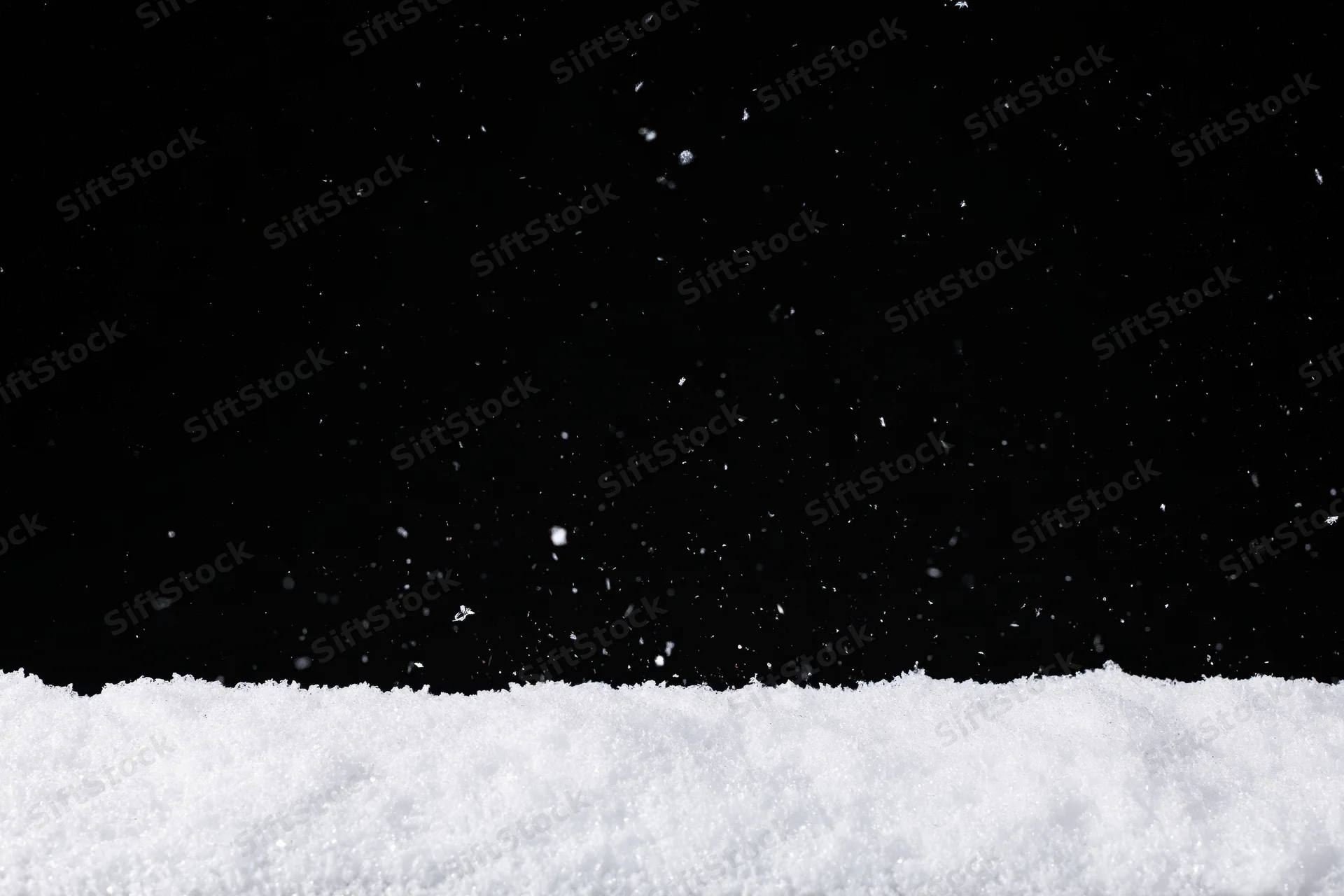 Close-up flat lay of white snow surface with falling flakes against black background