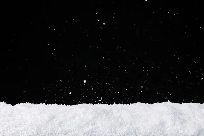 Close-up flat lay of white snow surface with falling flakes against black background