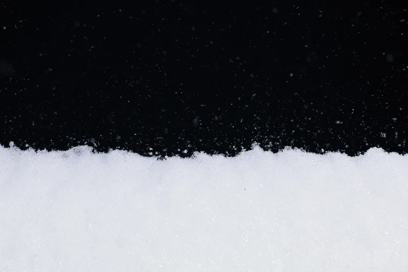 Close-up flat lay of white snow surface along the bottom edge against black background with falling snowflakes