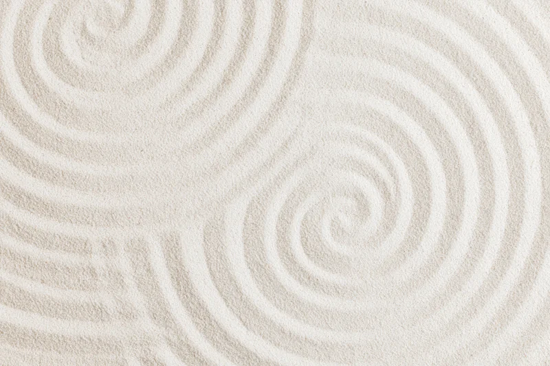 Raked white sand surface with spiral patterns in a zen garden setting