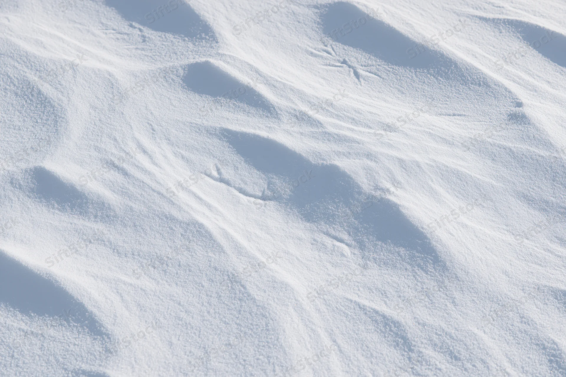 Close-up of undisturbed snow surface with soft ripples and shadows under sunlight