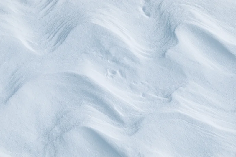 Close-up of undisturbed snow surface with soft ripples and waves filling the frame