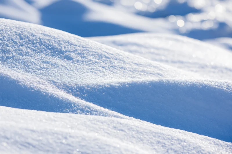 Close-up of wind-sculpted snow drifts under bright sunlight with blue shadows and sparkling highlights