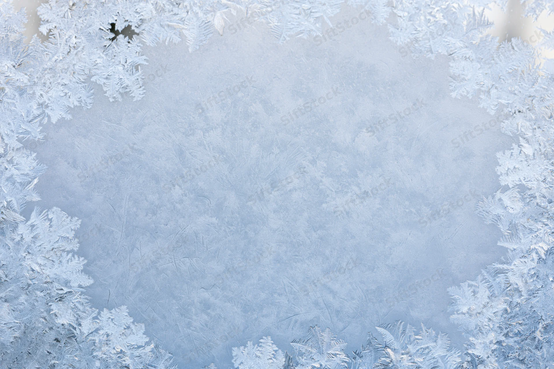 Frosted window pane with intricate ice patterns forming a border around a clear center