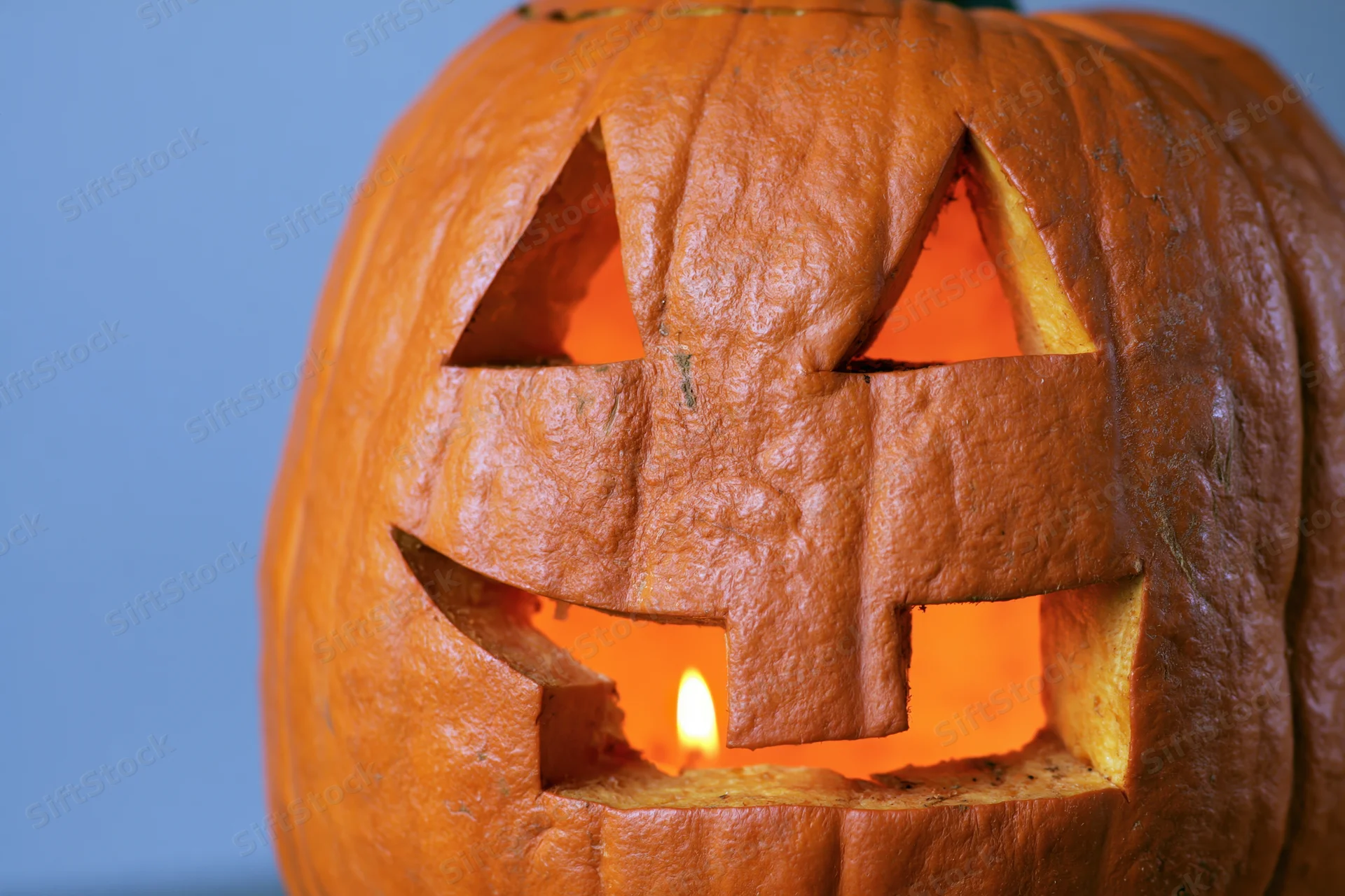 Carved pumpkin with glowing candle inside, set against blue background