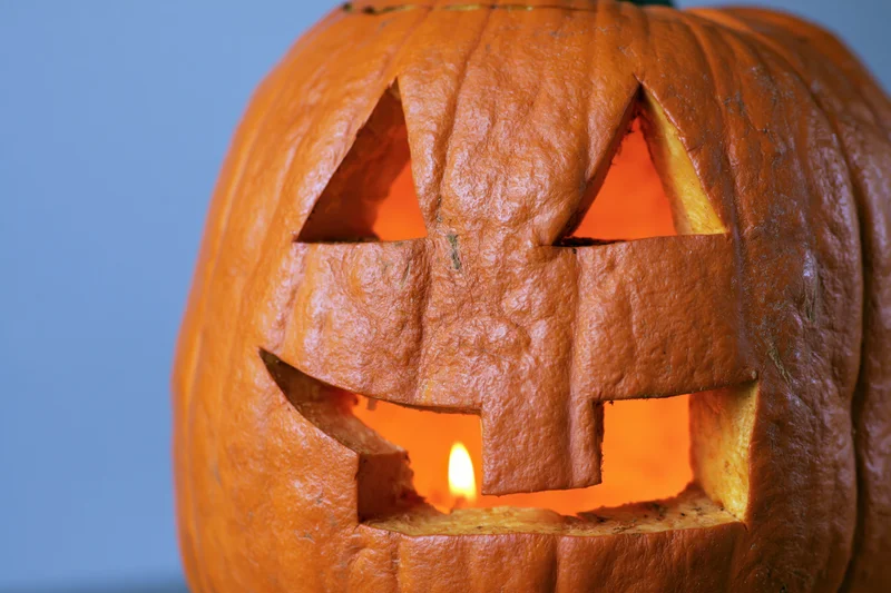 Carved pumpkin with glowing candle inside, set against blue background