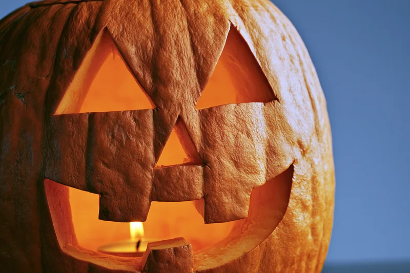 Carved pumpkin with glowing candle inside, close-up view against dark blue background