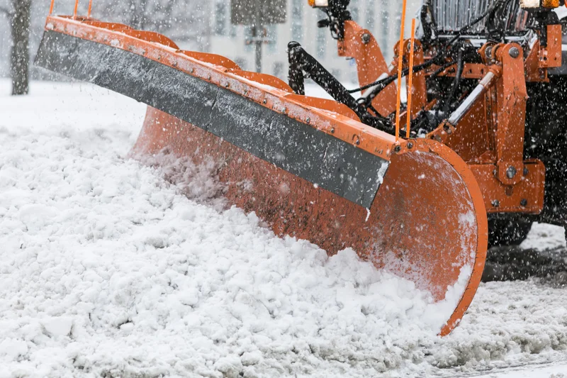 Large orange municipal snow plow blade pushing snow on a winter road