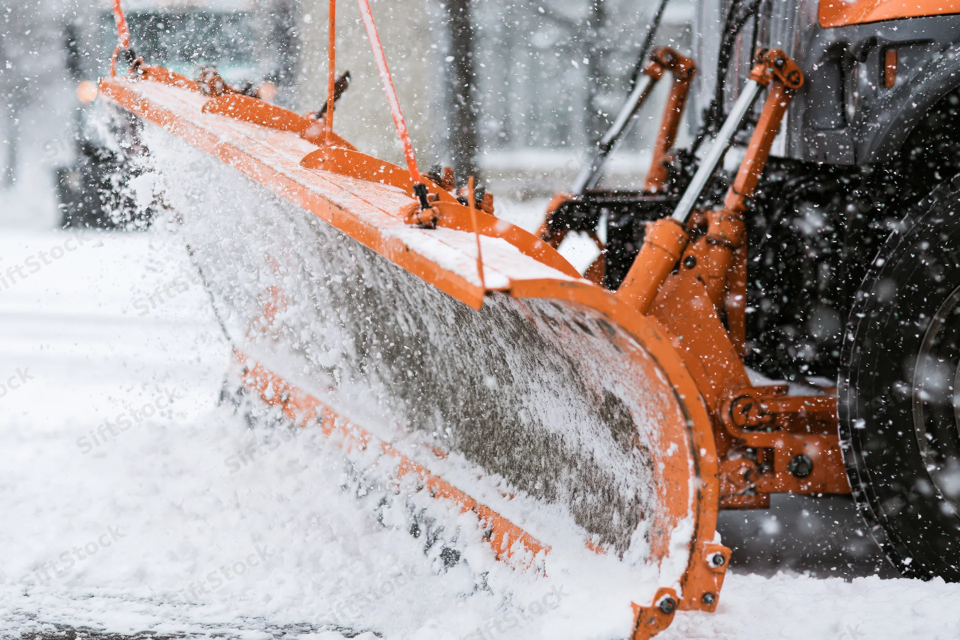 Orange municipal snow plow blade clearing snow from a road