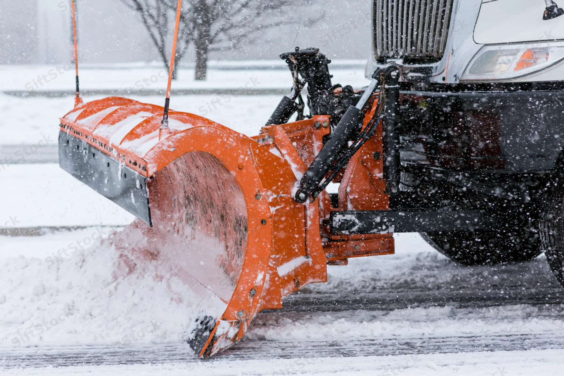Orange snowplow blade clearing snow from a road during a snowstorm