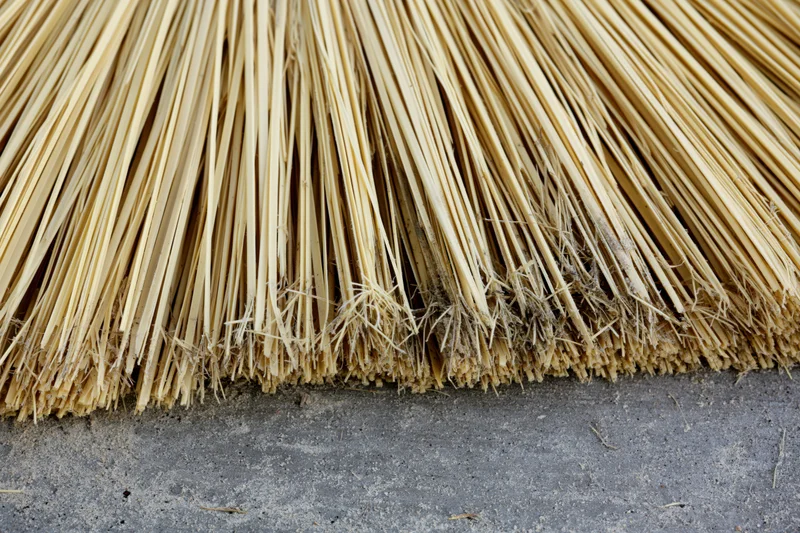 Close-up of worn broom bristles resting on a concrete floor