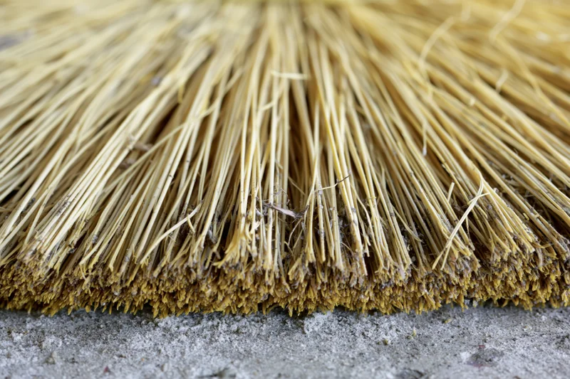 Close-up of worn broom bristles on a dusty floor