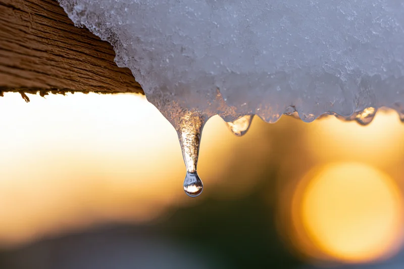 Icicle dripping from wooden roof eave at sunset