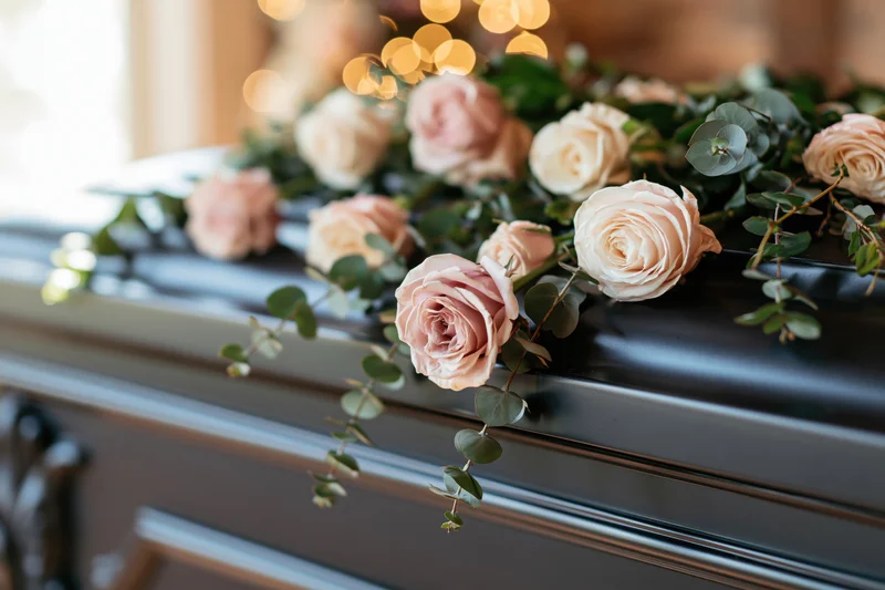 Pale pink and cream roses with eucalyptus sprigs arranged on a dark coffin lid