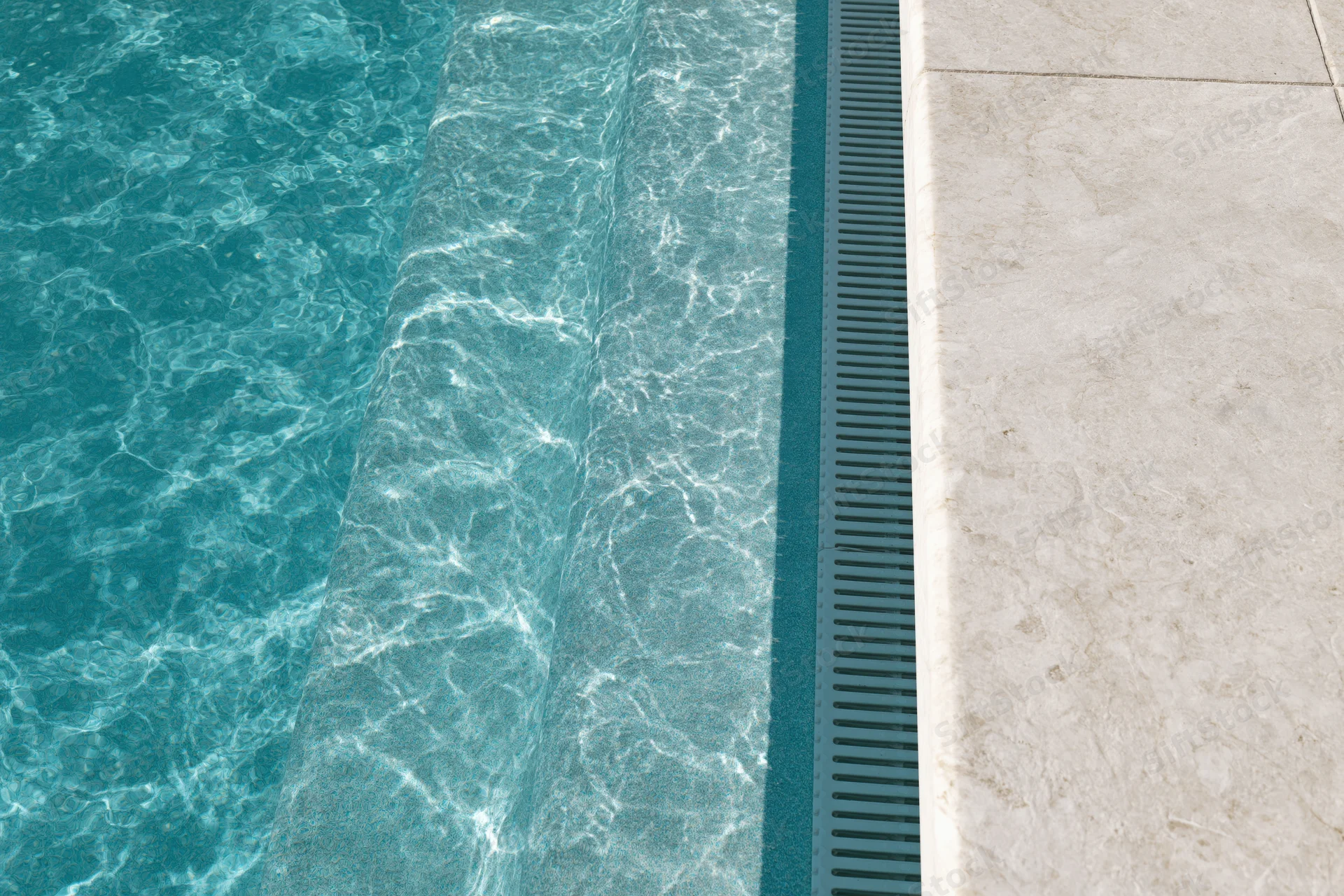 Overhead closeup of swimming pool edge with turquoise water and white marble tiles