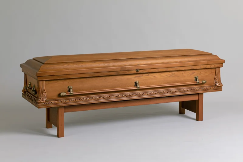 Wooden coffin with brass handles resting on matching stand against plain background