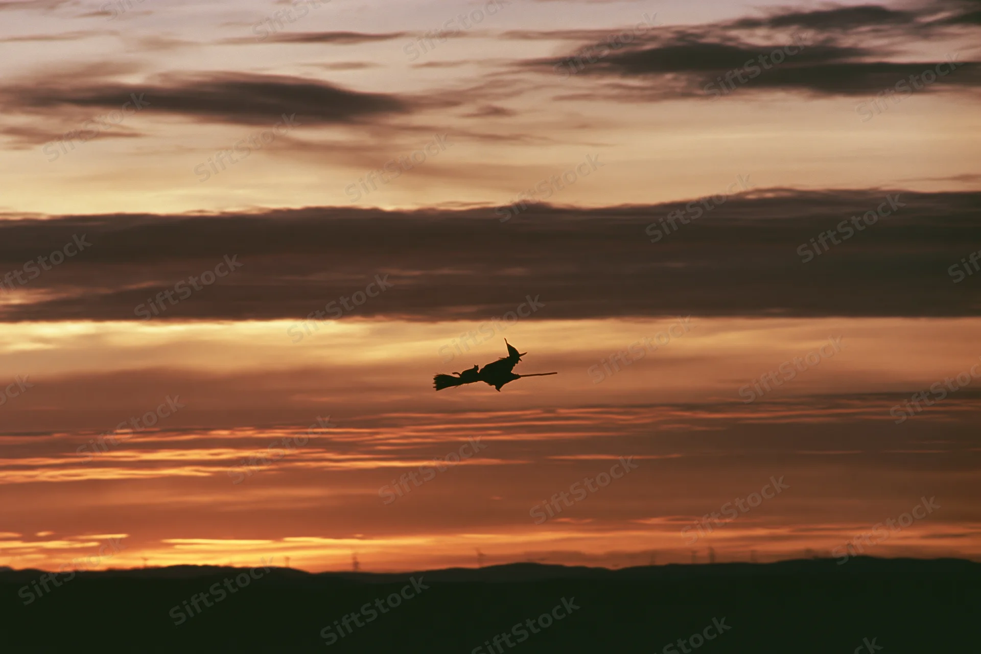 Witch flying on broom in silhouette against sunset sky