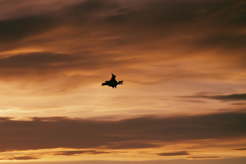 Silhouette of a witch riding a broomstick across a cloudy sunset sky