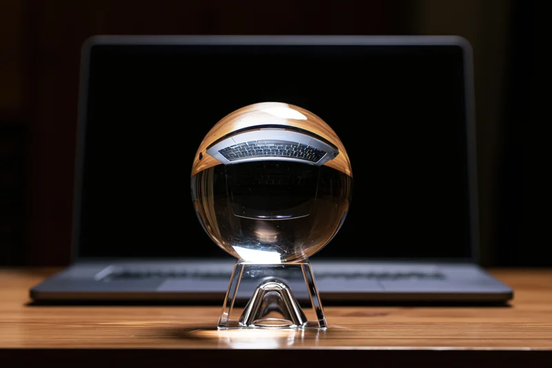Crystal ball on a glass stand in front of a laptop on a wooden desk