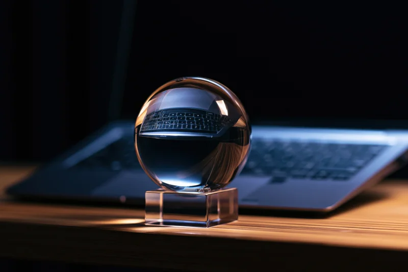 Crystal ball on glass stand reflecting laptop keyboard on wooden desk