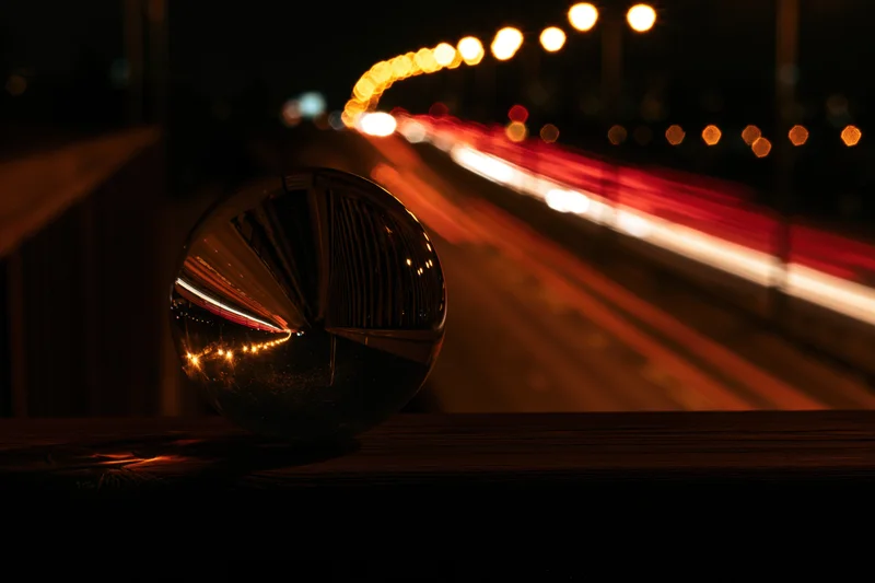 Crystal ball on wooden railing reflecting blurred city traffic at night