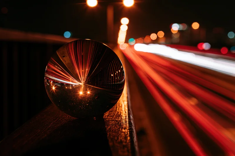 Crystal ball resting on wooden railing reflects city lights and moving traffic at night