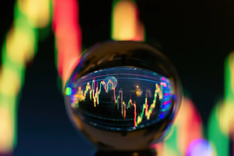 Crystal glass ball reflecting inverted stock market candlestick chart on dark background with colorful bokeh lights