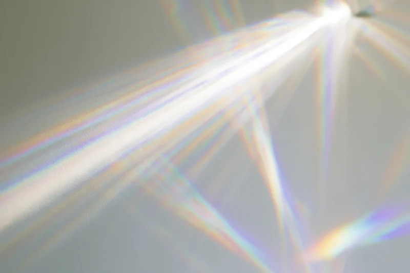 Light refraction pattern cast across a plain matte surface with rainbow spectrum and geometric beams