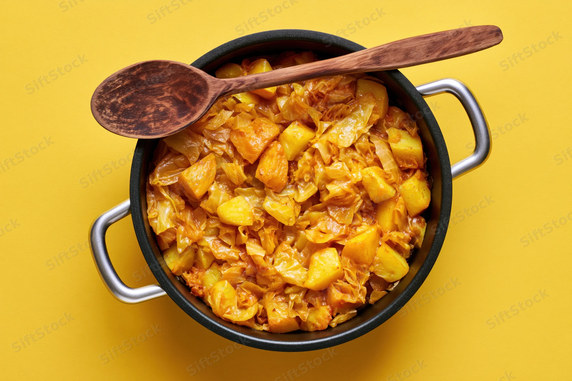 Braised cabbage and potato stew in a cast iron pot with wooden spoon on yellow background