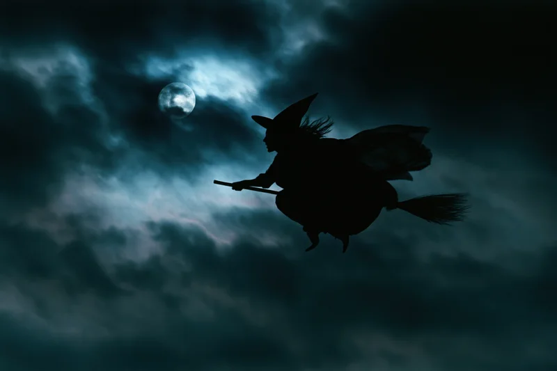 Witch flying on broomstick against moonlit cloudy sky