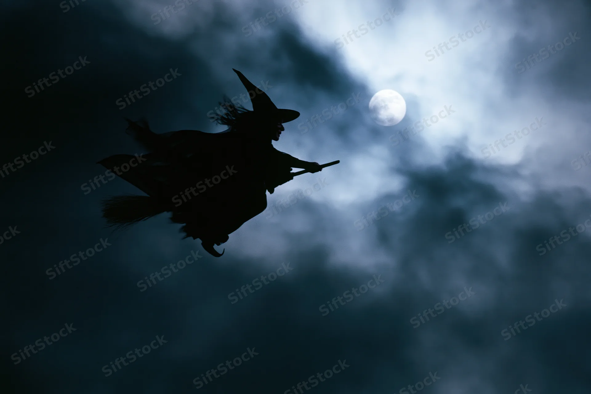 Witch flying on broomstick against moonlit cloudy sky