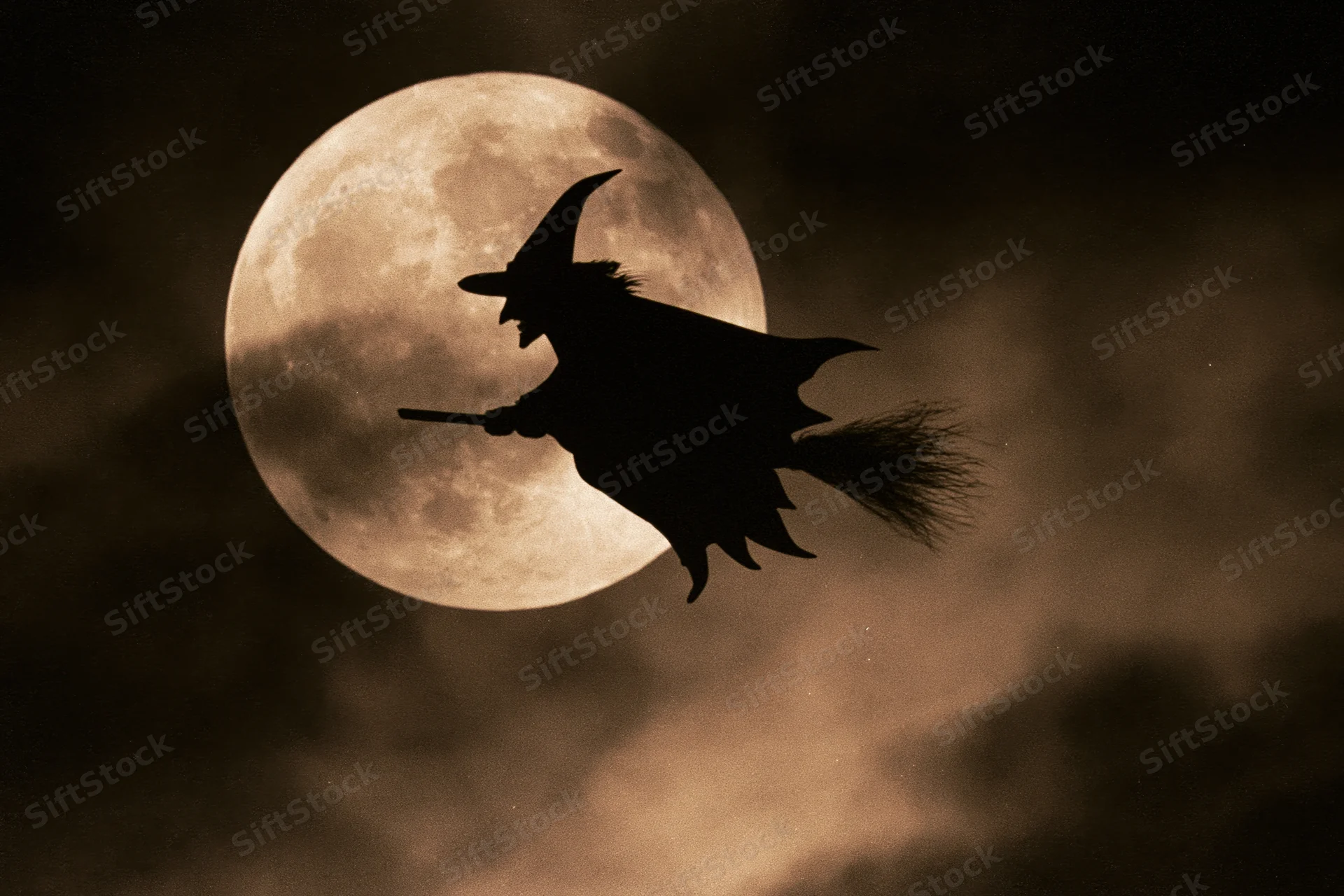 Witch flying on broomstick silhouetted against full moon in night sky