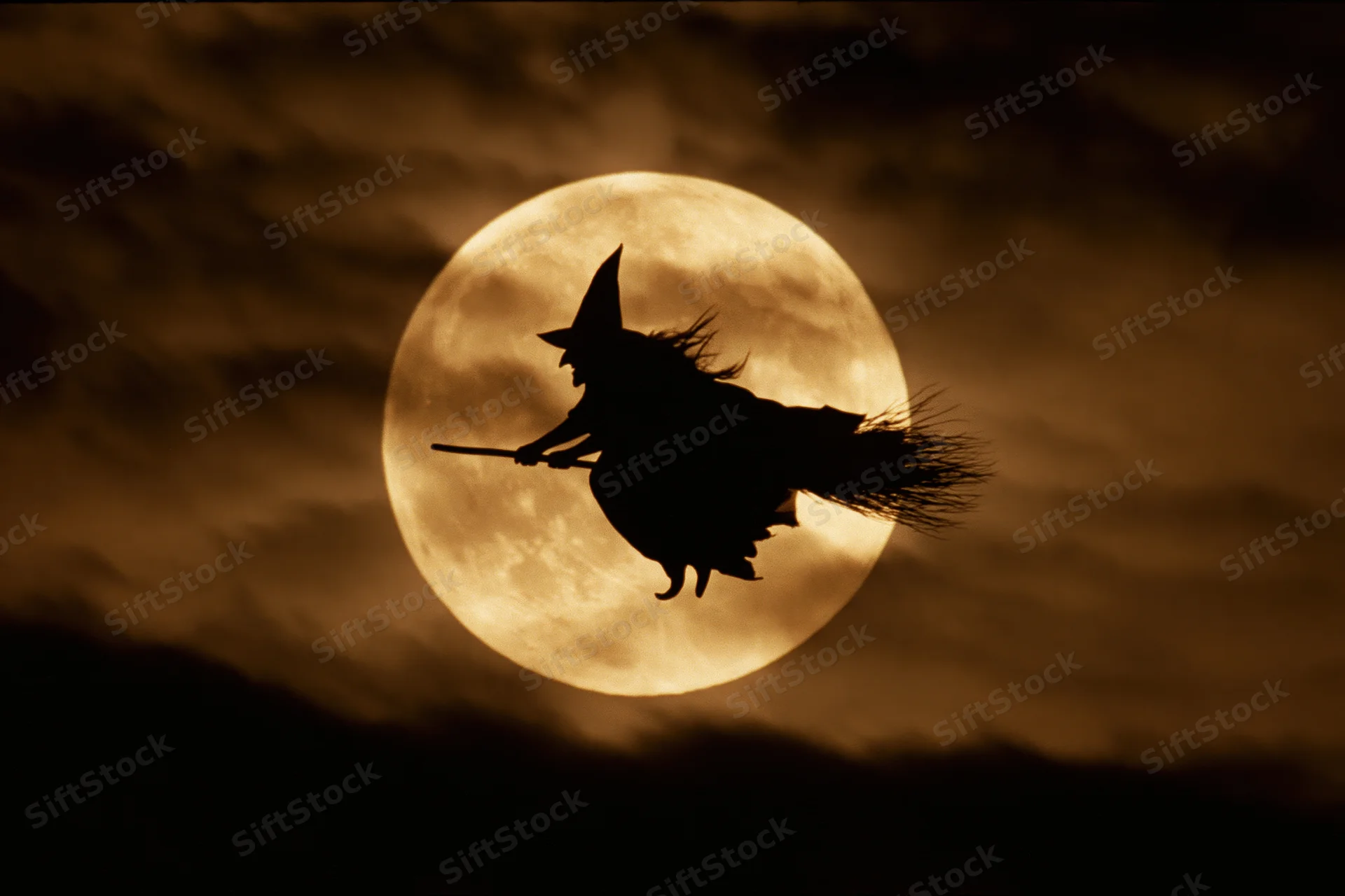 Witch flying on broomstick silhouetted against full moon in night sky