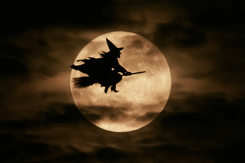 Witch flying on broomstick silhouetted against full moon in night sky