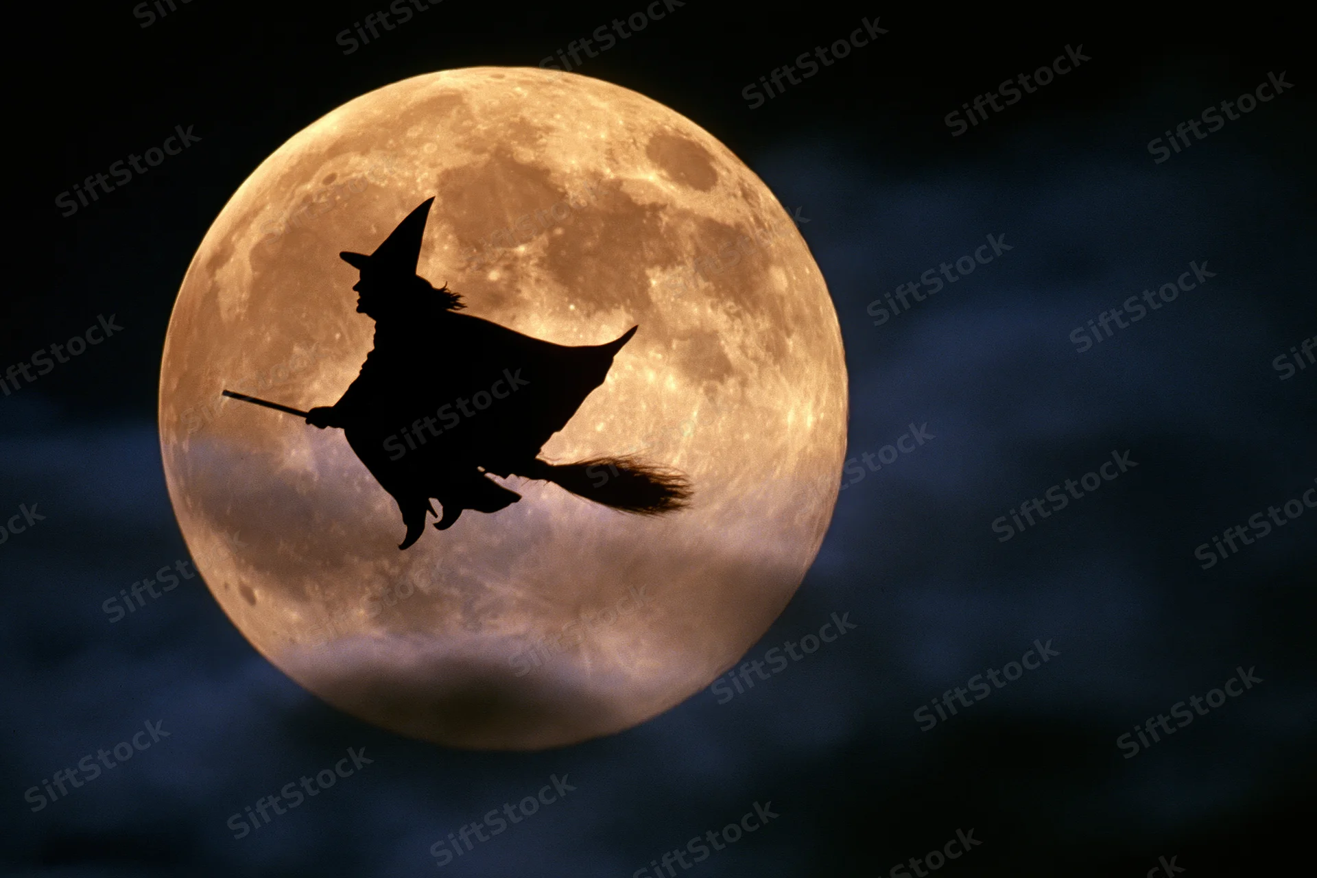 Witch flying on broomstick silhouetted against full moon in night sky