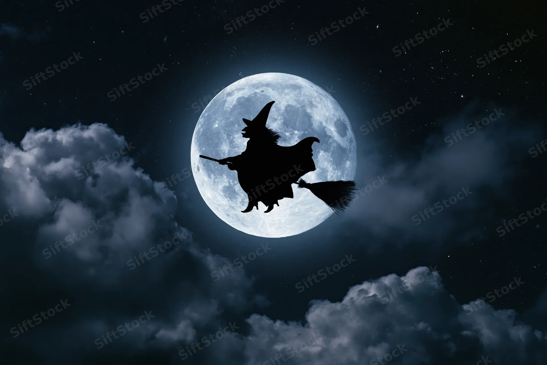 Witch flying on broomstick silhouetted against full moon in starry night sky with clouds