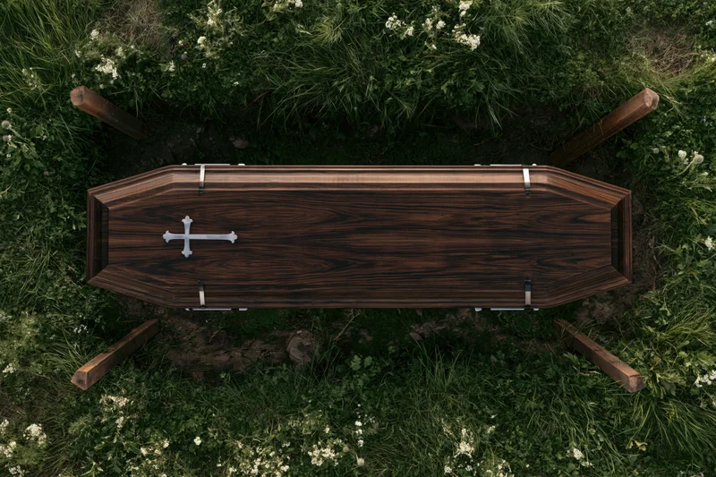 Dark walnut wooden coffin with silver cross and metal bands resting on grass in cemetery, overhead view